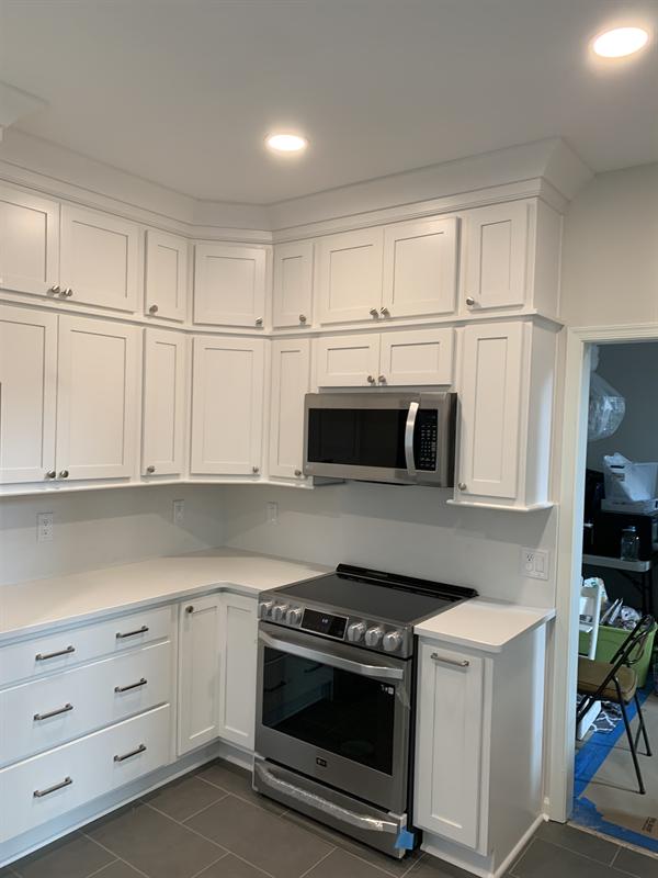 White corner kitchen cabinets with crown molding around a range and microwave