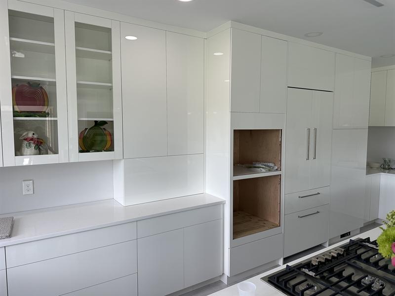 White high-gloss wall cabinets with glass-front doors and a panel-ready refrigerator