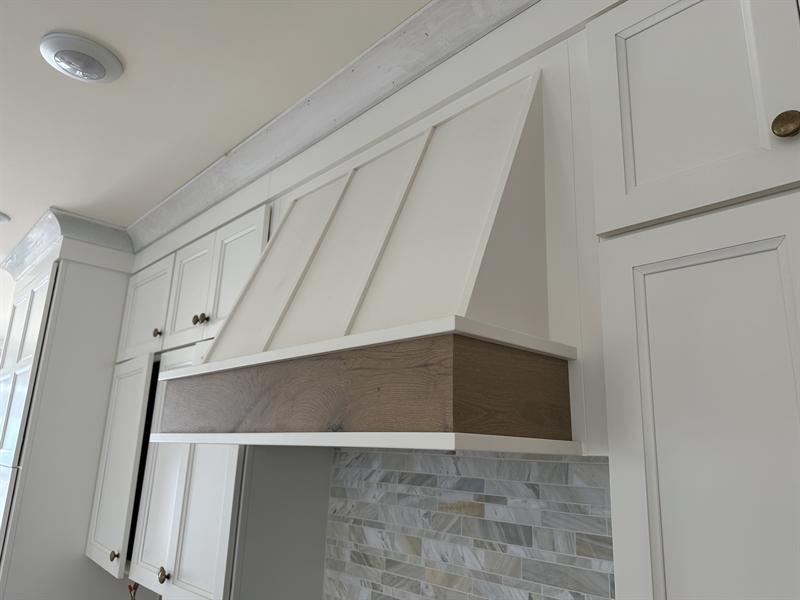 Custom white range hood surround with a wood accent band and crown molding