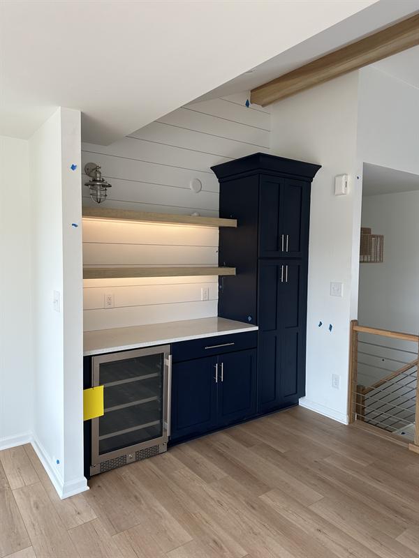 Navy blue bar cabinets with floating shelves and a beverage fridge