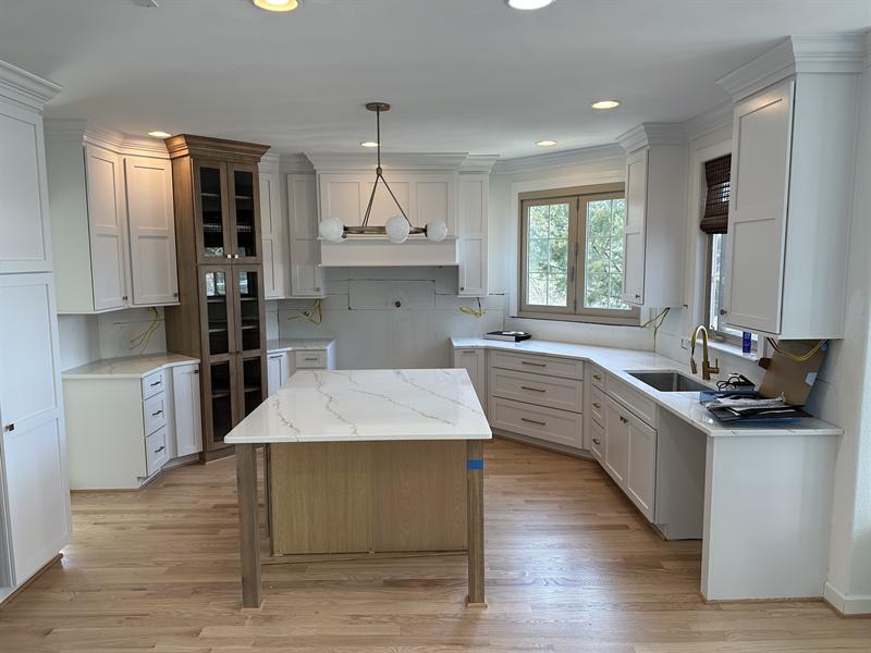 White shaker kitchen cabinets with a stained glass-front hutch and a light oak island